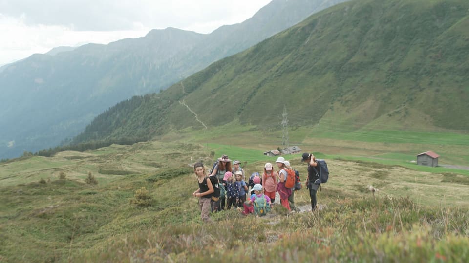 Kinder stehen auf einer Wiese vor einem Bergpanorama.