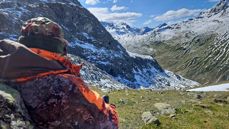 Person in Tarnkleidung blickt auf schneebedeckte Berglandschaft.