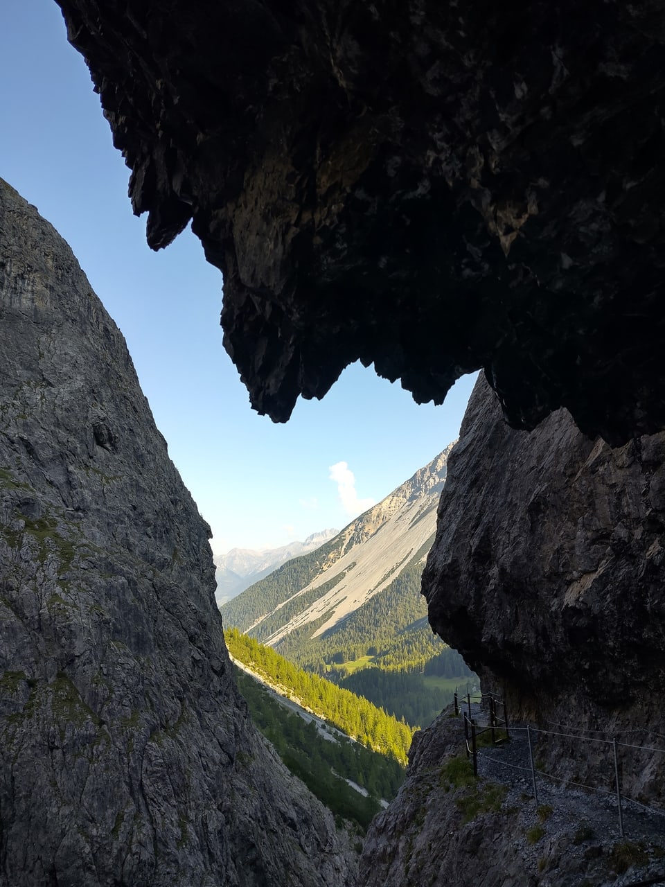 Blick durch eine Felsformation auf ein grünes Tal mit Bergen im Hintergrund.