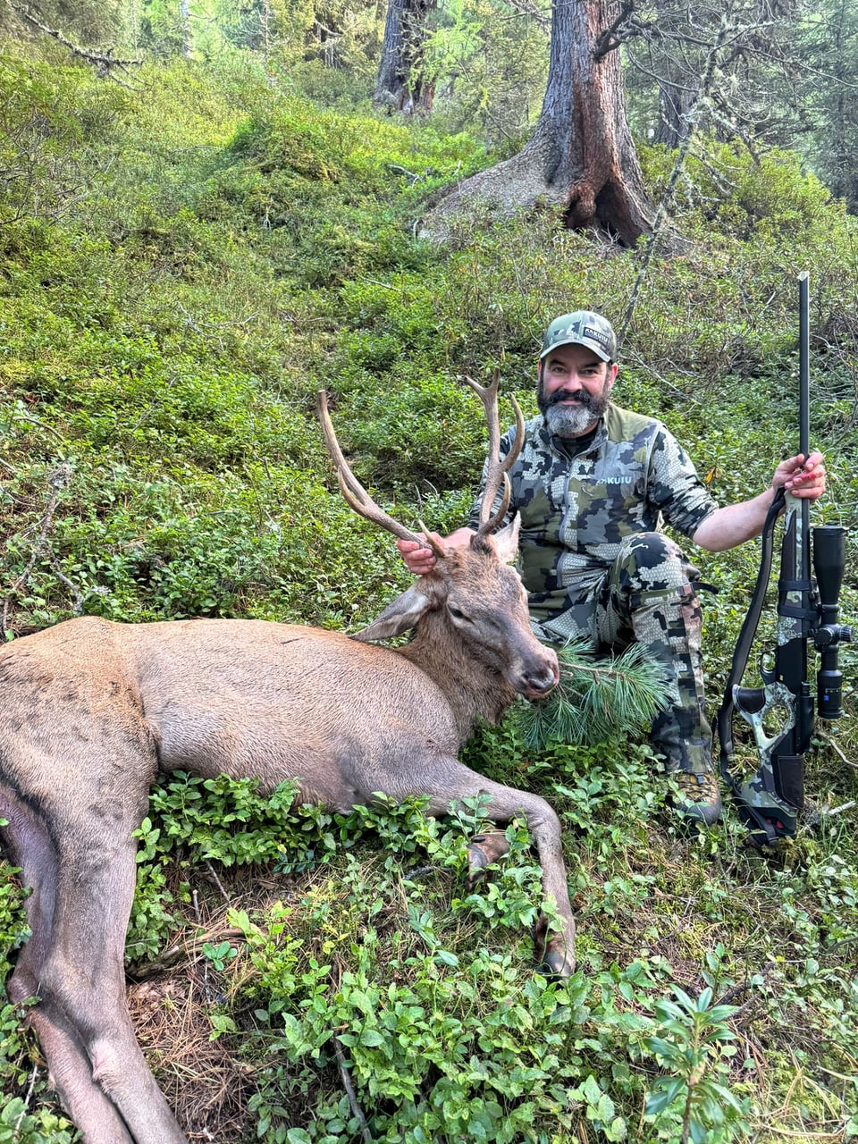 Jäger im Wald mit erlegtem Hirsch und Schusswaffe.