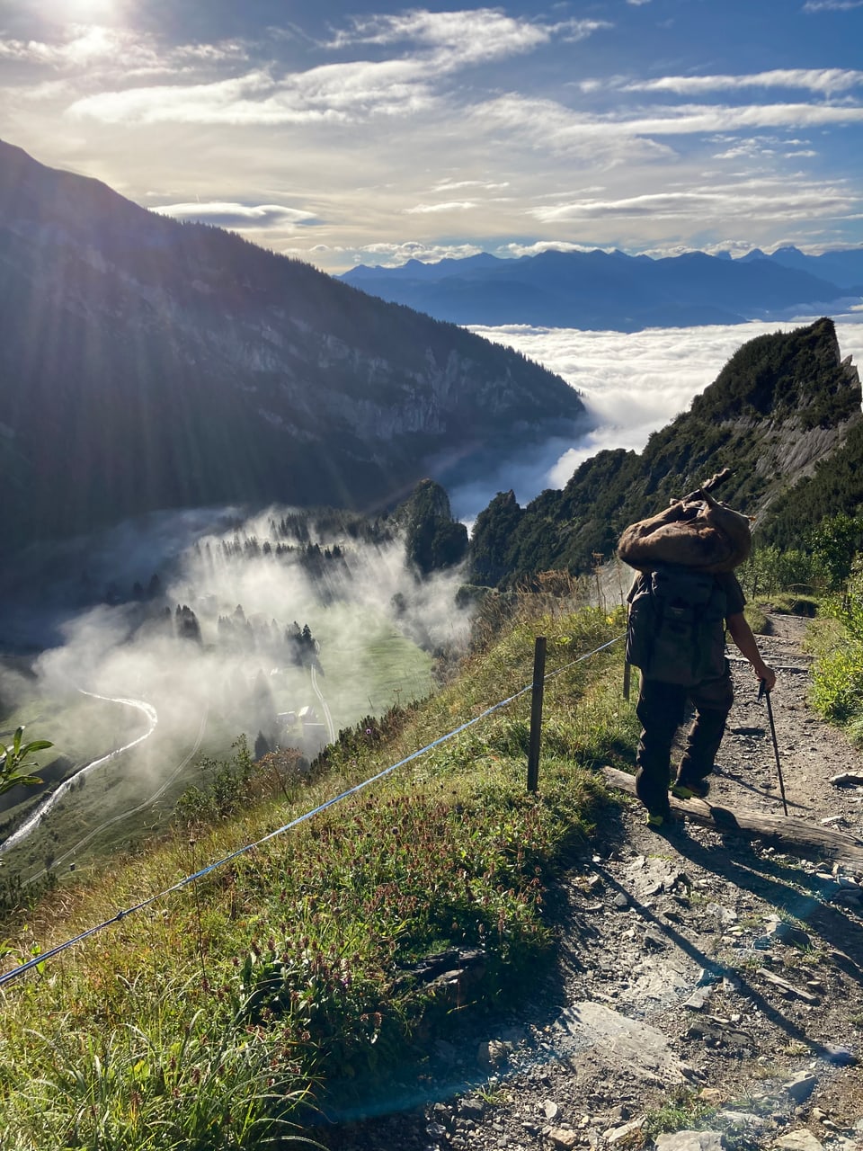 Wanderer auf Bergpfad mit Nebel im Tal darunter.