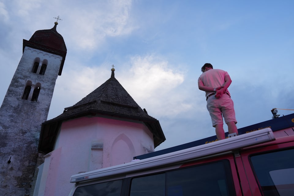 Mann steht auf einem Auto vor einer Kirche bei Sonnenuntergang am Open Air Lumnezia 2024.