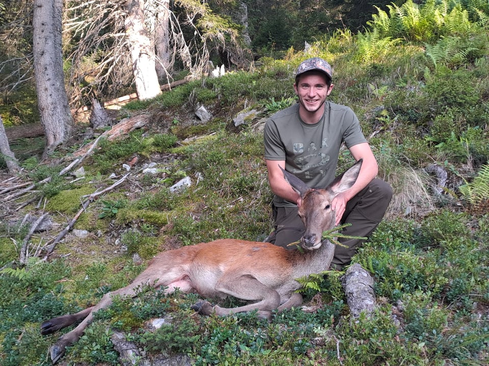 Mann in Wald kniend neben einem Hirsch.