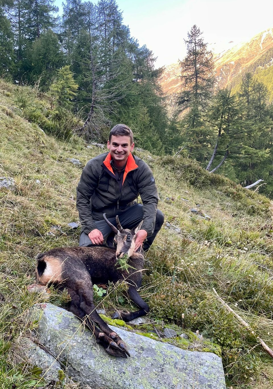 Mann kniet neben erlegtem Wild im Gebirge.