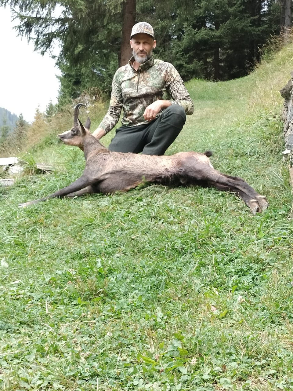 Jäger kniet neben erlegtem Reh auf einer Wiese.