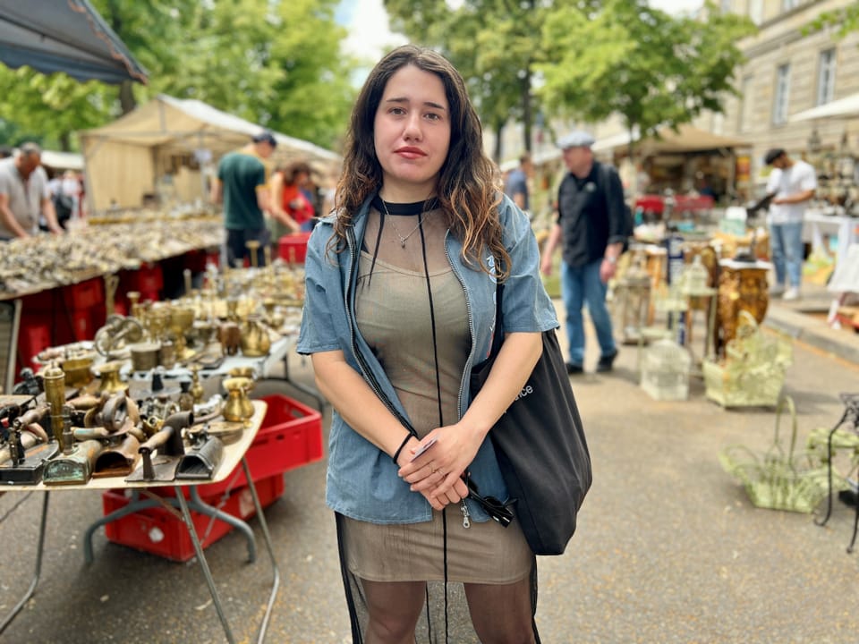 Frau auf einem Flohmarkt mit Antiquitätenständen im Hintergrund.