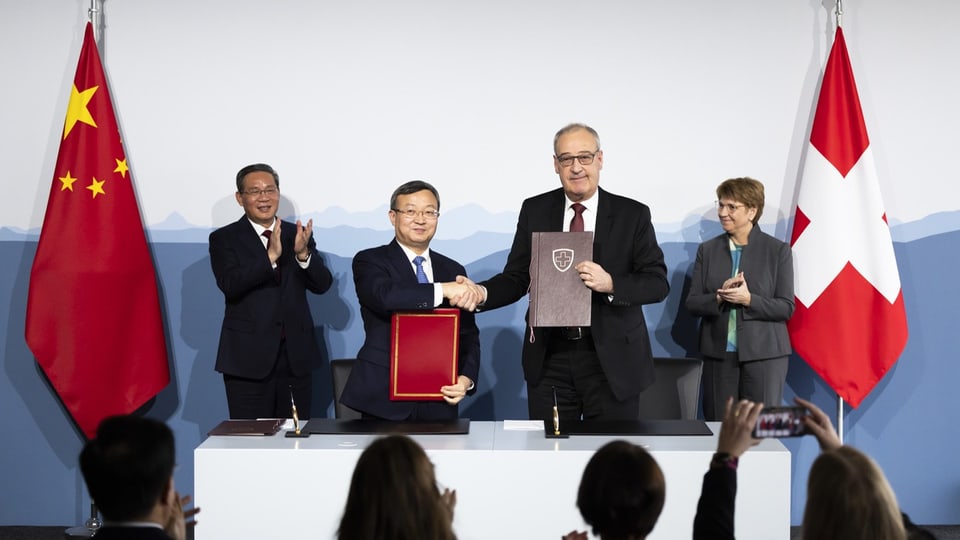 Bundesrat Guy Parmelin und der chinesische Premierminister Li Qiang halten jeweils eine Mappe in die Höhe.