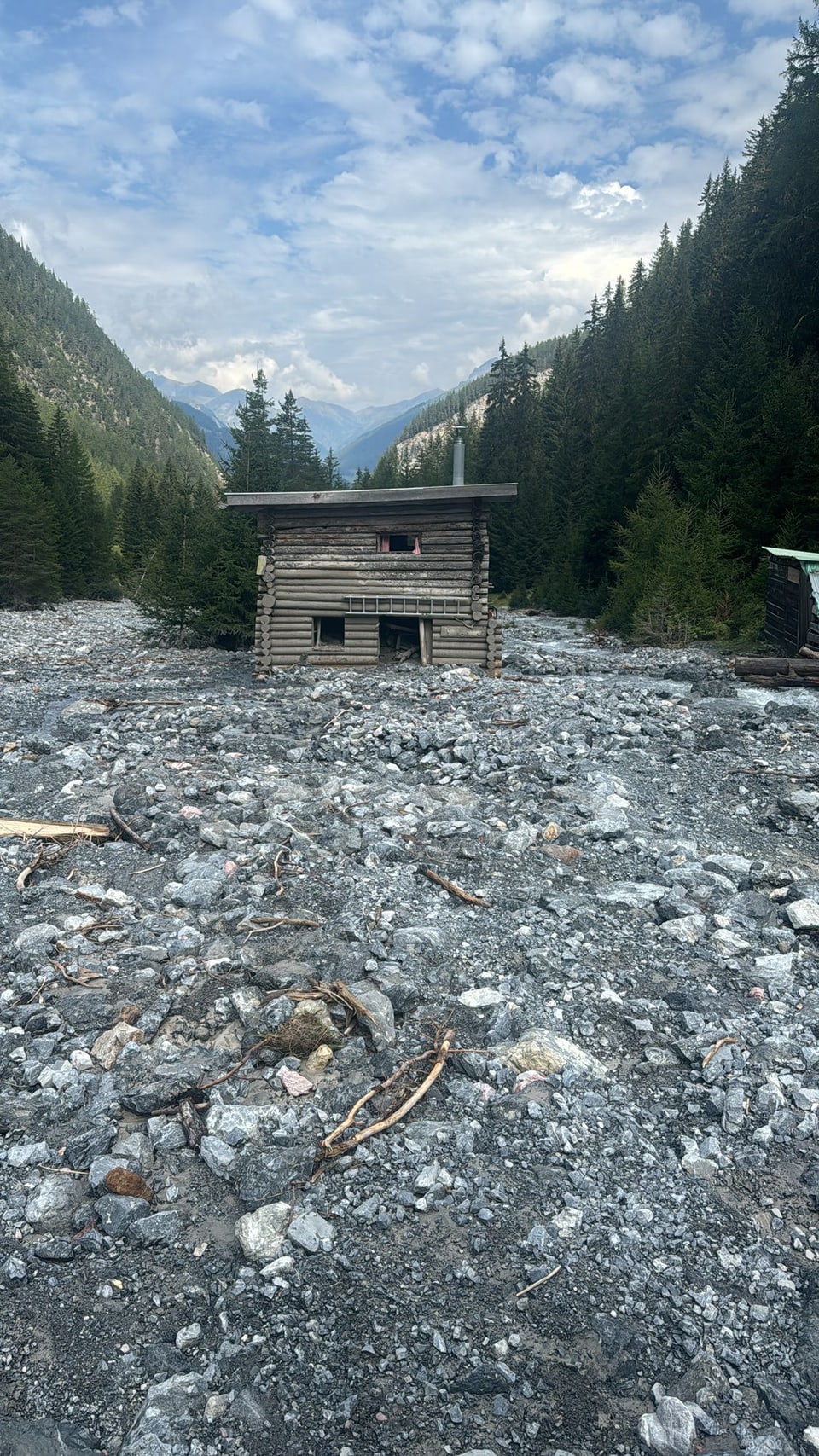 Altes Holzhaus in einem felsigen Tal, umgeben von bewaldeten Bergen.