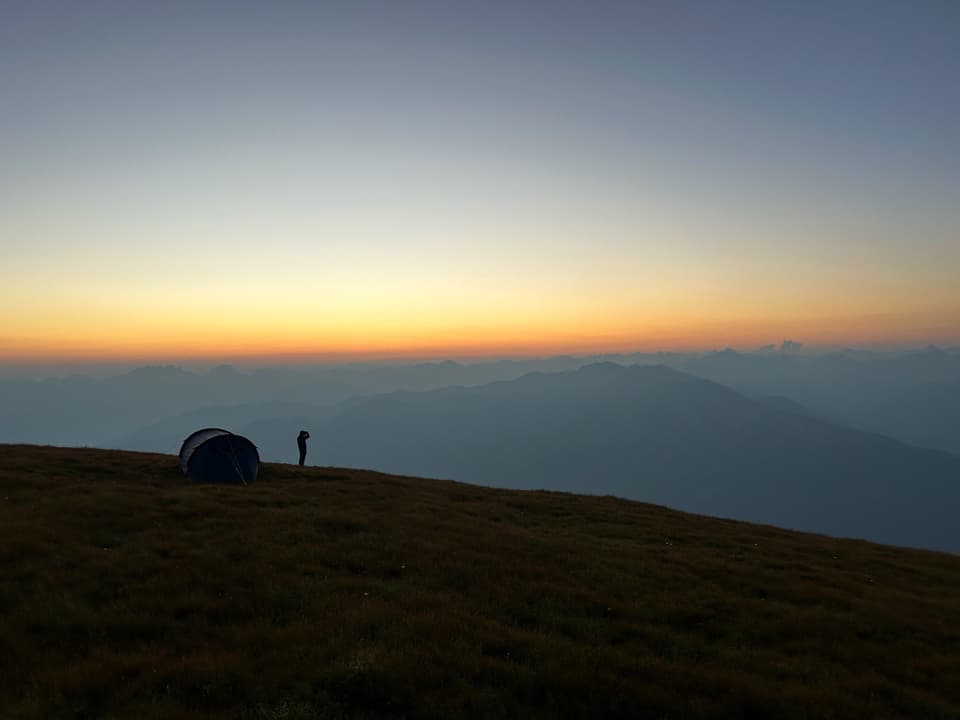 Zelt auf einer Bergwiese bei Sonnenaufgang.