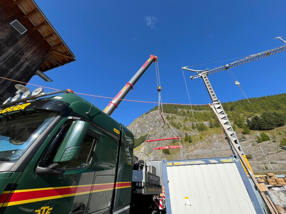 Lkw mit Kran hebt Last an Baustelle in bergiger Landschaft.