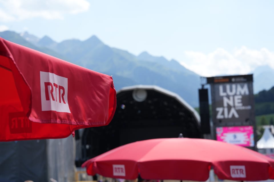 Rote RTR-Sonnenschirme vor Festivalbühne und Bergen im Hintergrund.