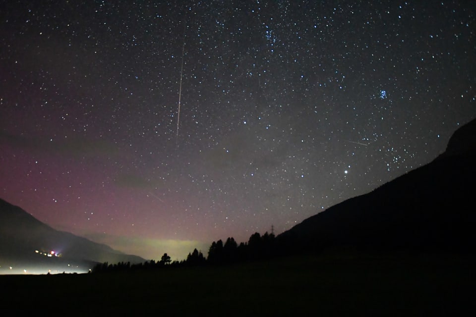 Sternenhimmel mit Polarlichtern über einer Berglandschaft.