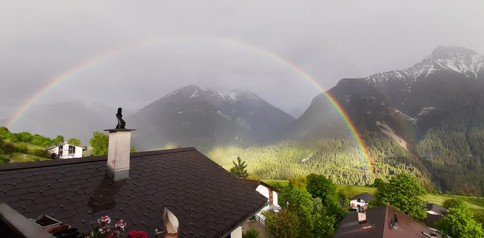 Regenbogen über Berglandschaft und Häusern.