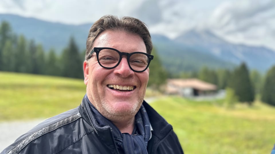 Lächelnder Mann mit Brille im Freien vor Berglandschaft.