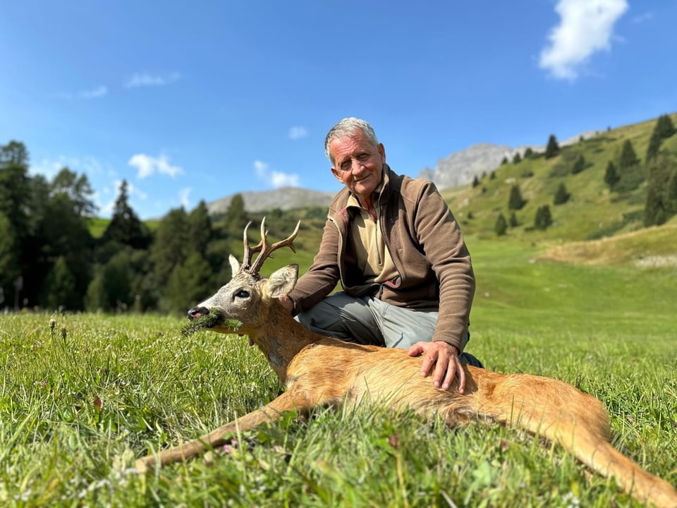 Mann mit erlegtem Hirsch auf einer Wiese in den Bergen.