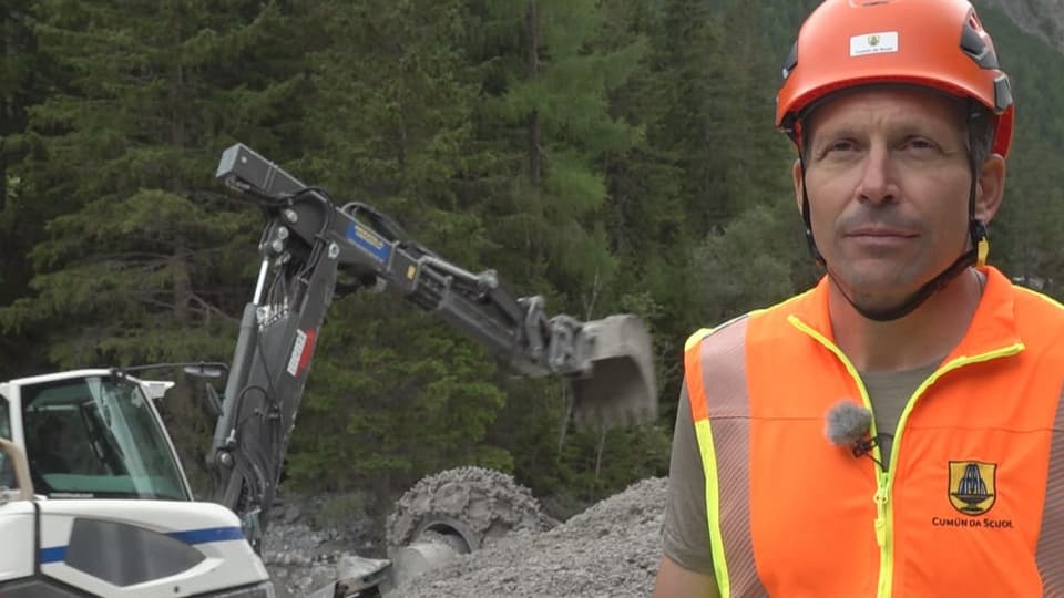 Bauarbeiter mit orangener Schutzkleidung und Schutzhelm vor Bagger im Wald.