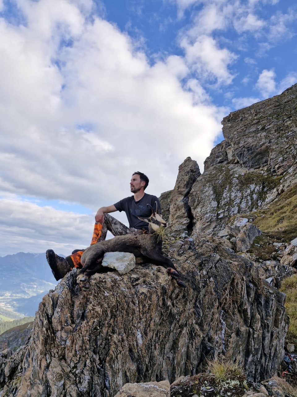 Mann sitzt auf Felsen in Bergen mit totem Tier.