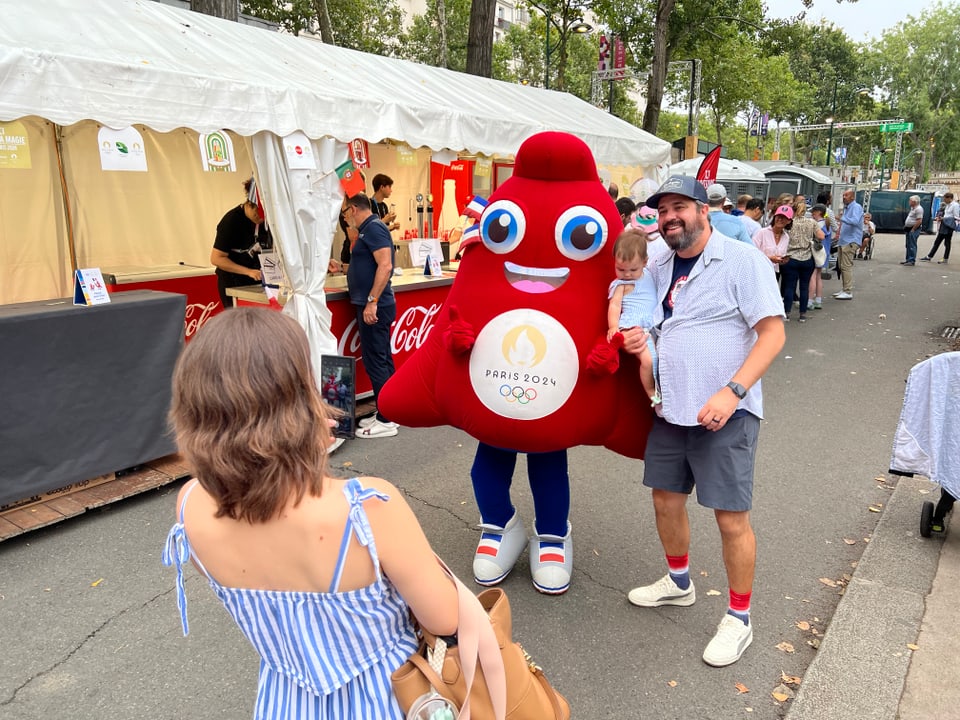 Paris2024: Personen lassen sich mit dem Olympiamaskottchen fotografieren.