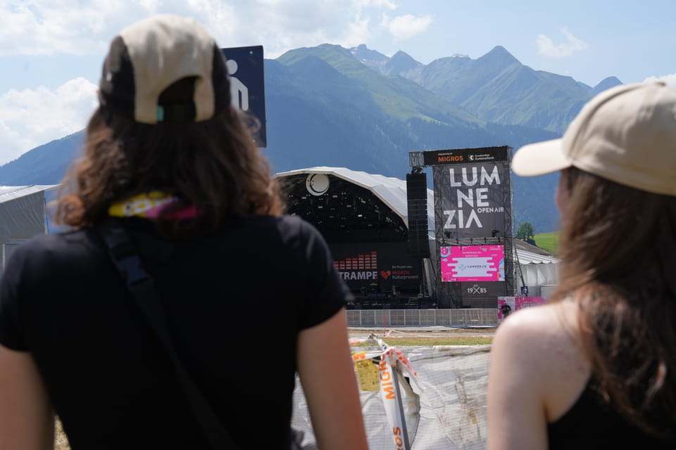 Zwei Personen vor einer Open-Air-Bühne mit Bergkulisse am Open Air Lumnezia 2024.