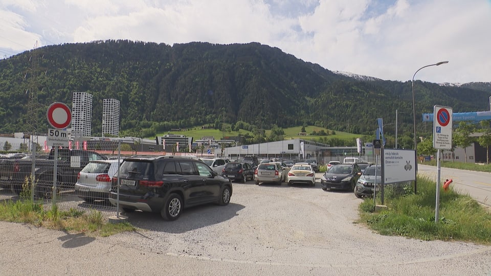 Parkplatz mit Autos und Bergen im Hintergrund.
