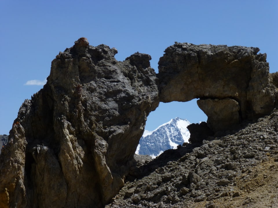 Felsen mit Loch und schneebedeckter Berg im Hintergrund.