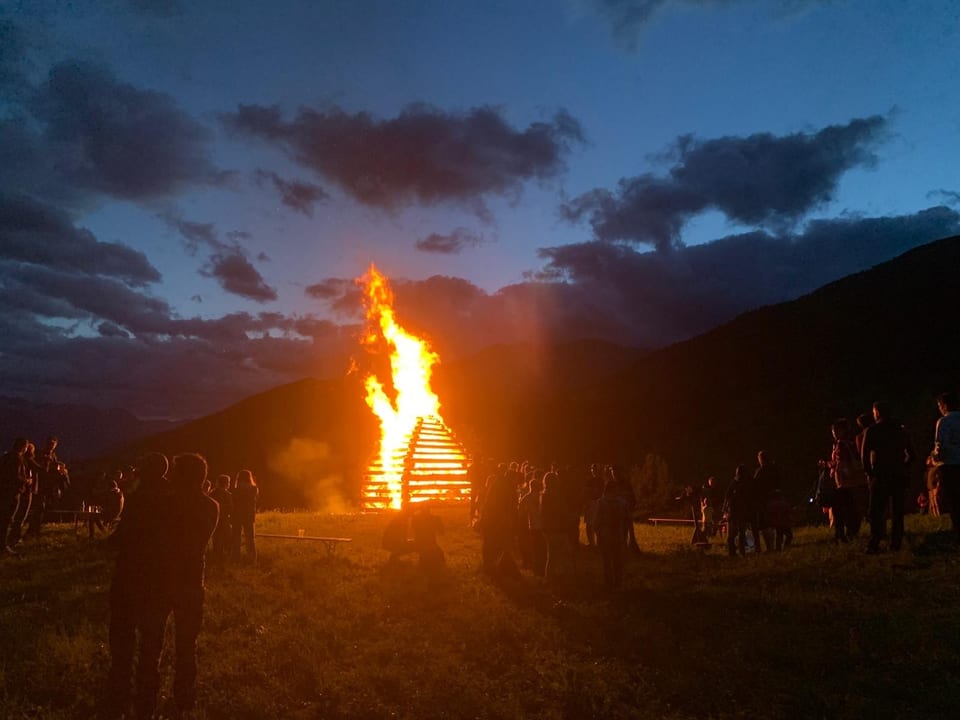 Menschen um ein grosses Lagerfeuer bei Sonnenuntergang.