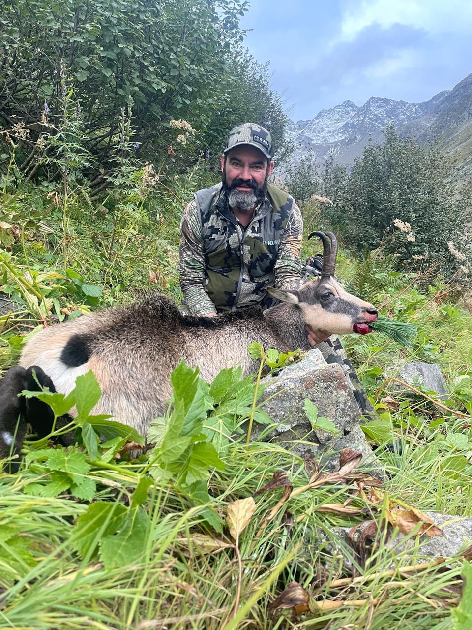 Jäger posiert mit totem Steinbock in Berglandschaft.