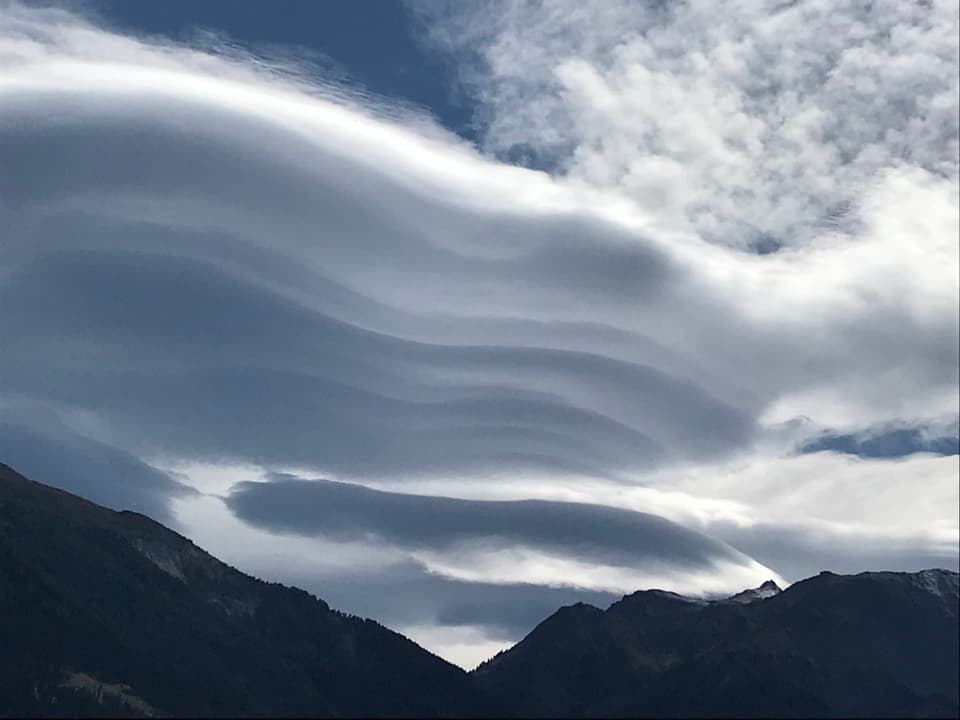 Wellenförmige Wolken über Bergen.