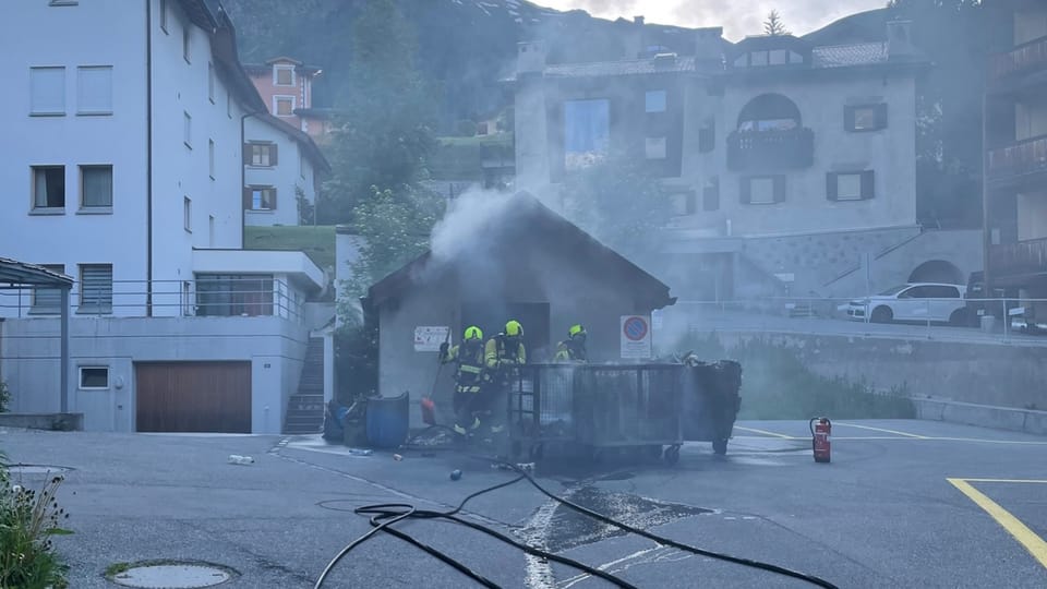 Feuerwehrleute löschen brennende Mülltonnen auf einer Strasse.