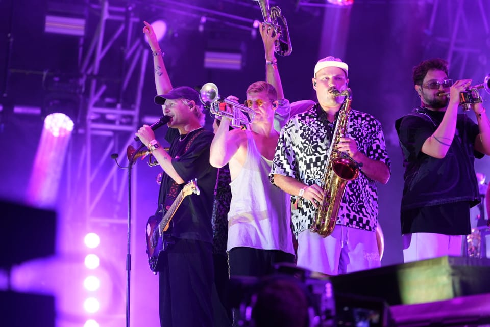 Bandmitglieder spielen Blasinstrumente auf einer Bühne in violettem Licht am Open Air Lumnezia 2024..