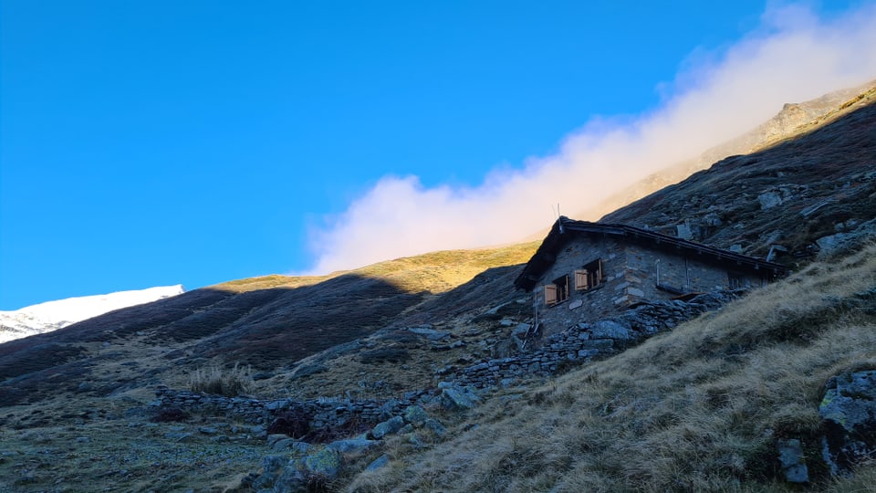 Steinhütte auf einem Grasbewachsenen Hügel unter klarem Himmel.