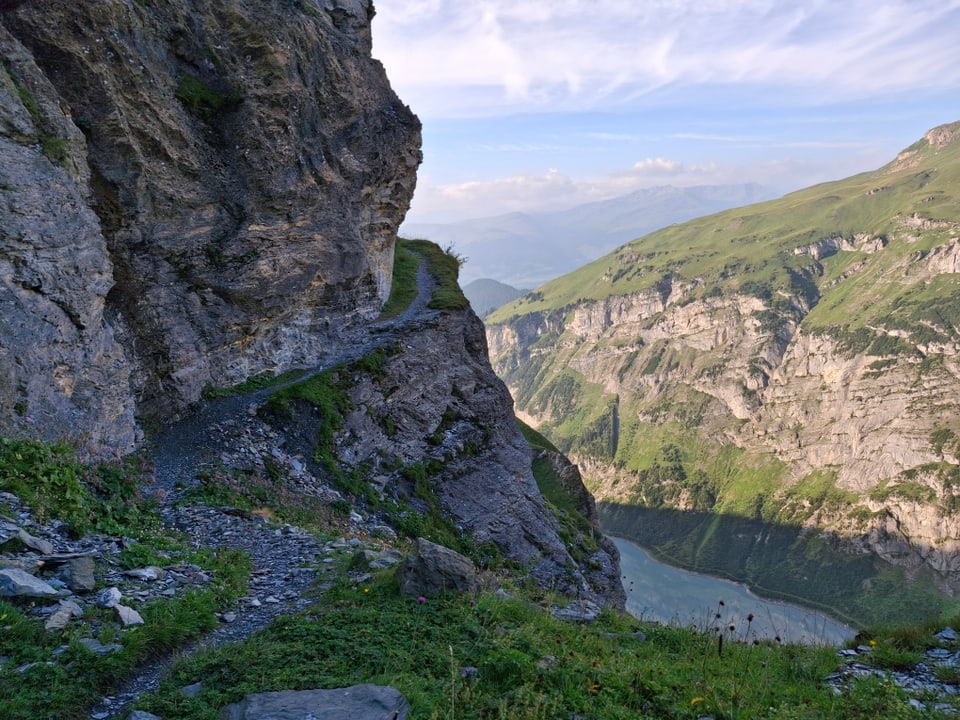 Schmaler Bergpfad entlang einer Klippe mit Blick auf ein Tal und Berge.