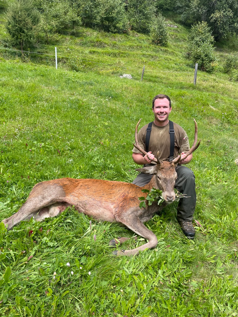 Jäger posiert mit erlegtem Hirsch auf einer Wiese.