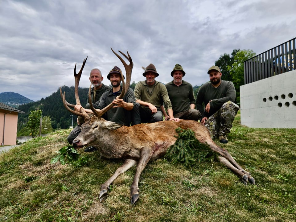 Fünf Männer posieren mit erlegtem Hirsch auf einer Wiese.