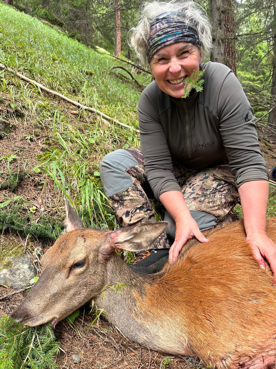 Frau neben einem liegenden Hirsch im Wald.