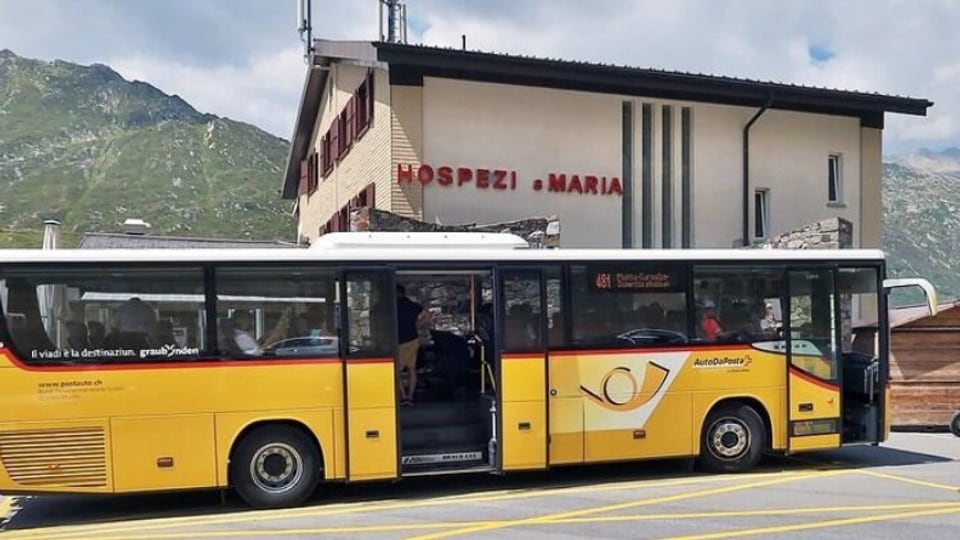 Gelber Bus vor Hospiz mit Bergen im Hintergrund.