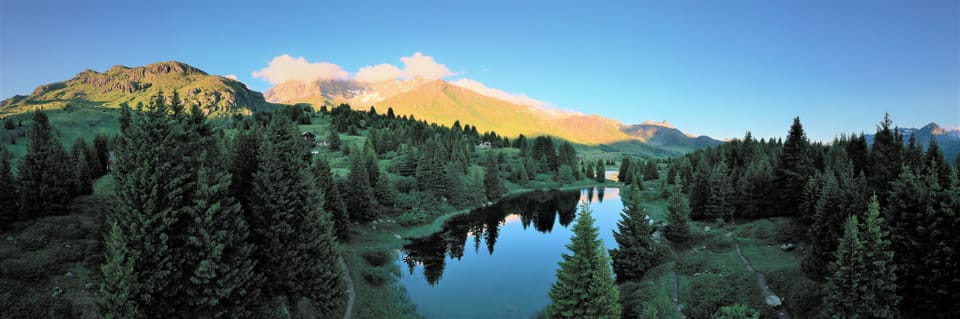 Panorama einer Berglandschaft mit See und Wald.