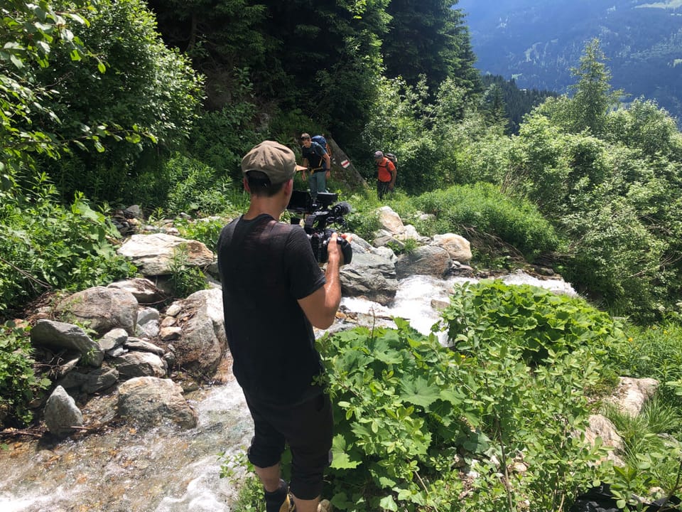 Person filmt in der Natur auf einem bewaldeten Bergweg.