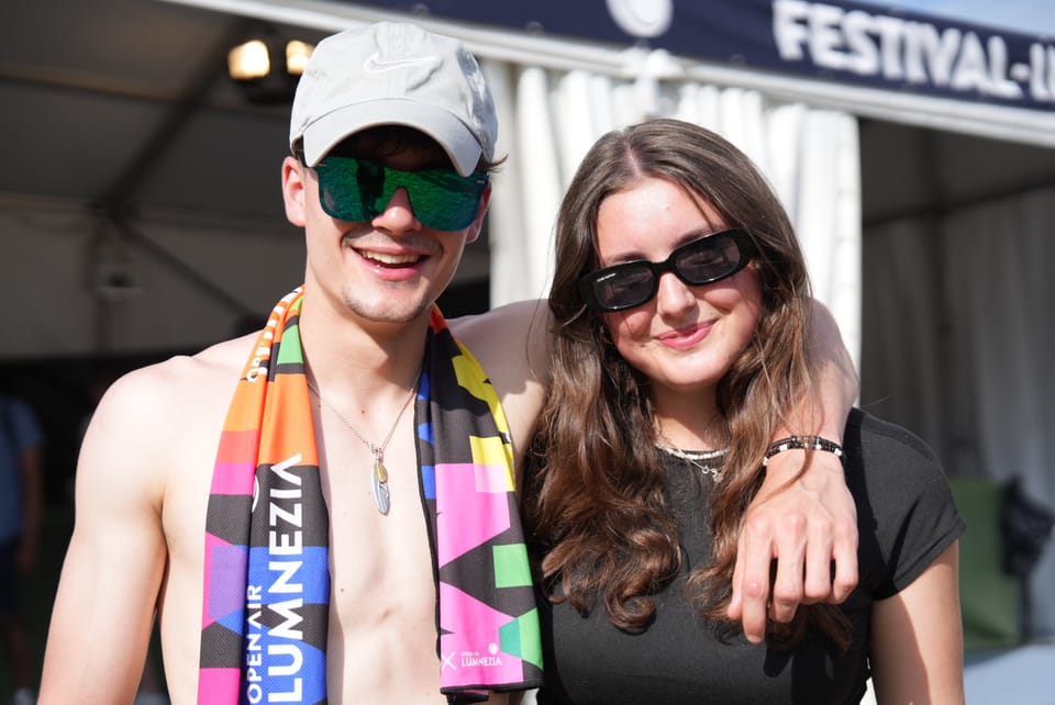 Zwei junge Menschen mit Sonnenbrillen vor einem Festzelt am Open Air Lumnezia 2024..