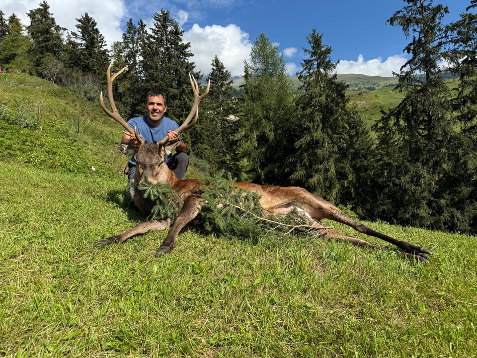 Mann posiert mit erlegtem Hirsch im Wald.