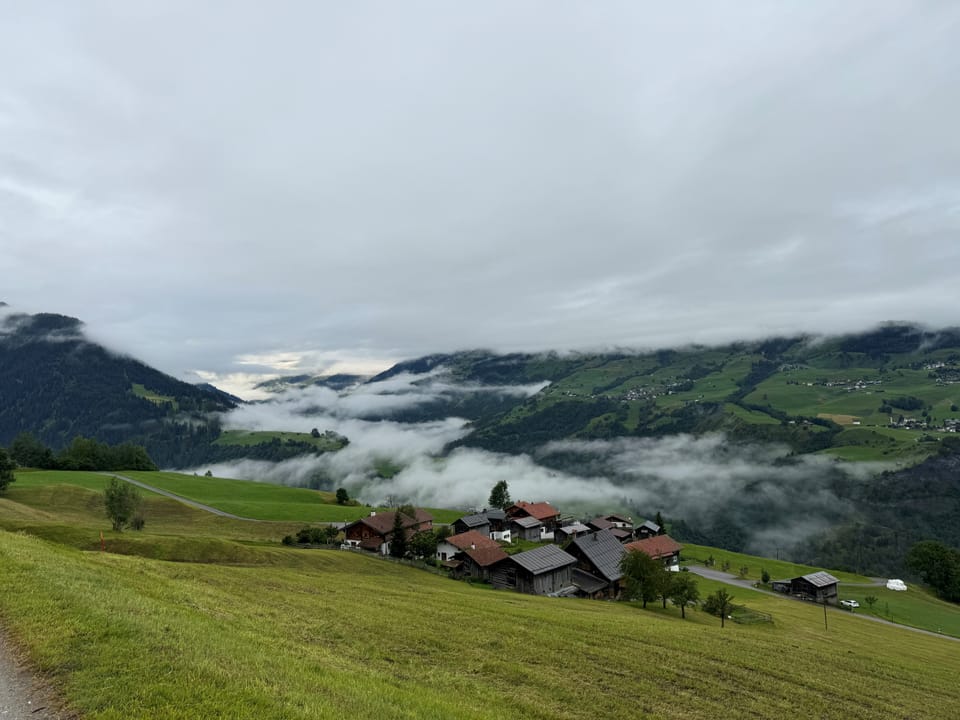 Blick über nebelverhangene Hügel und Dörfer in einer bergigen Landschaft.