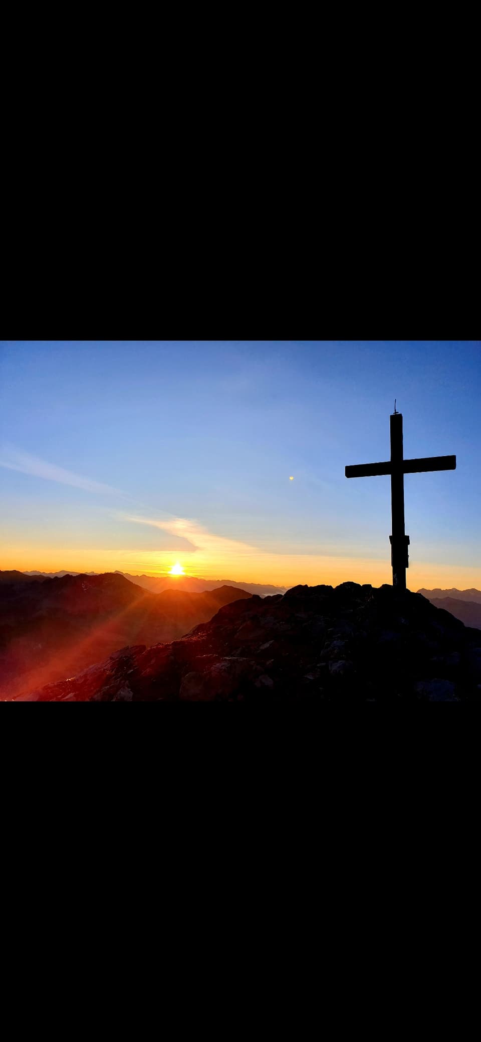 Ein Gebirgskreuz mit einer tiefstehenden Sonne.