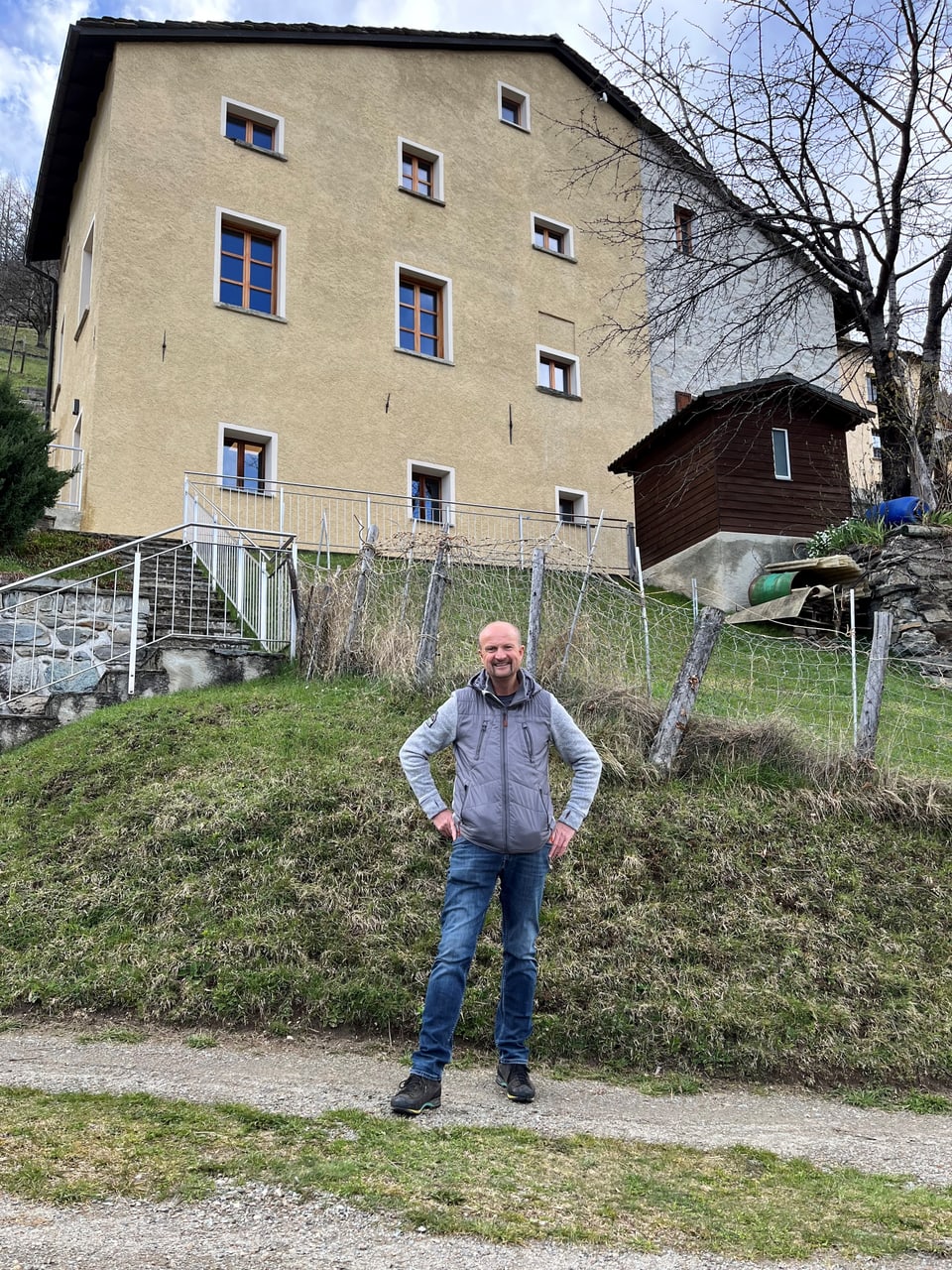 Mann steht vor einem Haus auf einem grasbewachsenen Hügel.