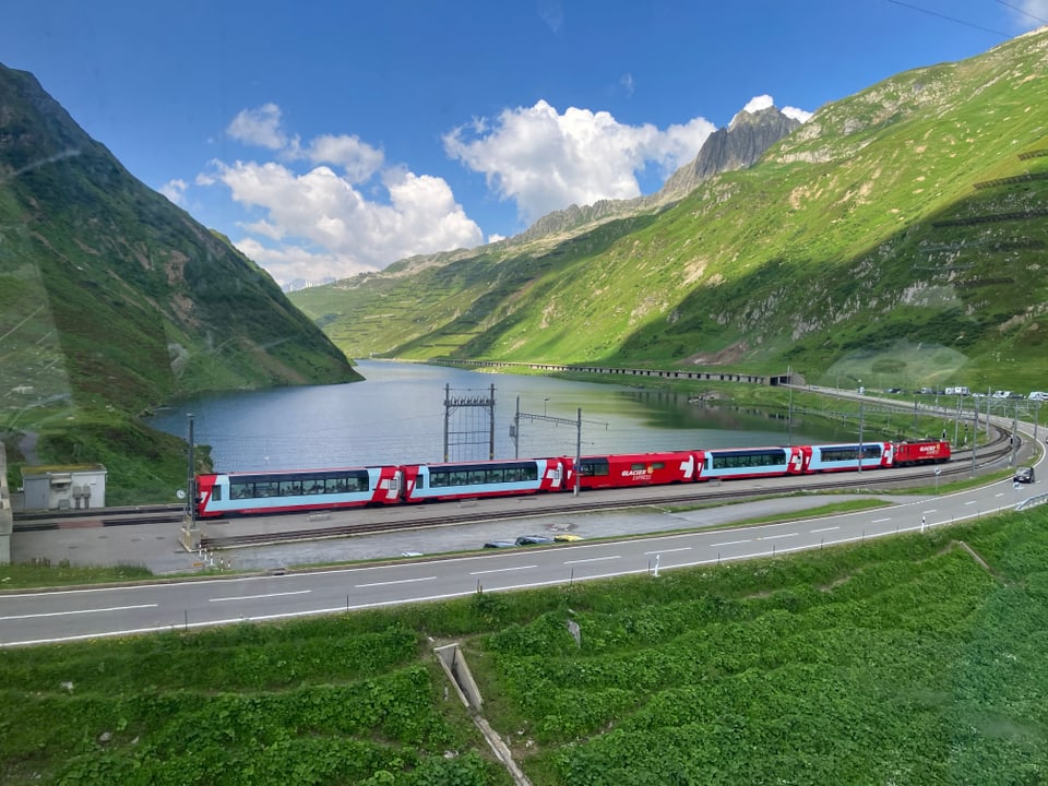 Panoramaaufnahme eines roten Zuges in einer Berglandschaft mit See.