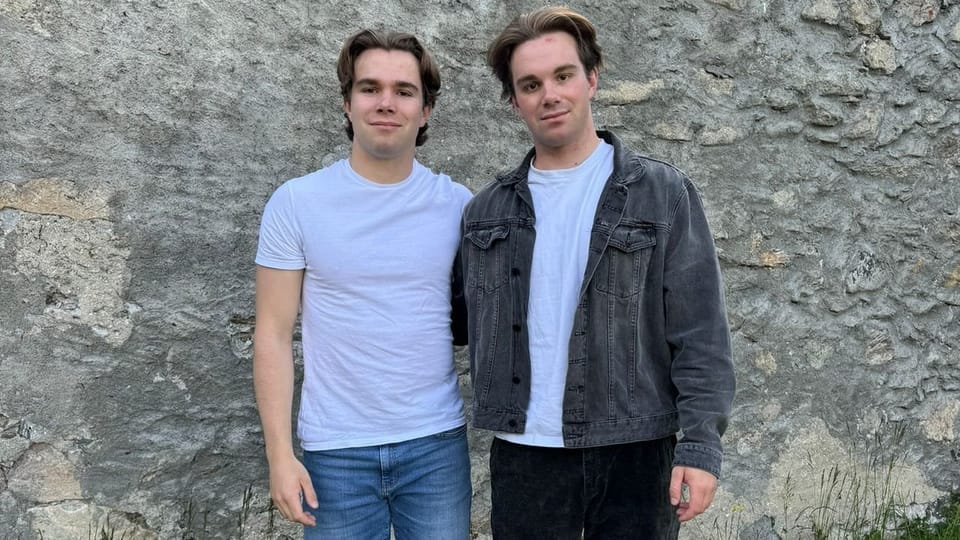 Zwei junge Männer vor einer Steinmauer.