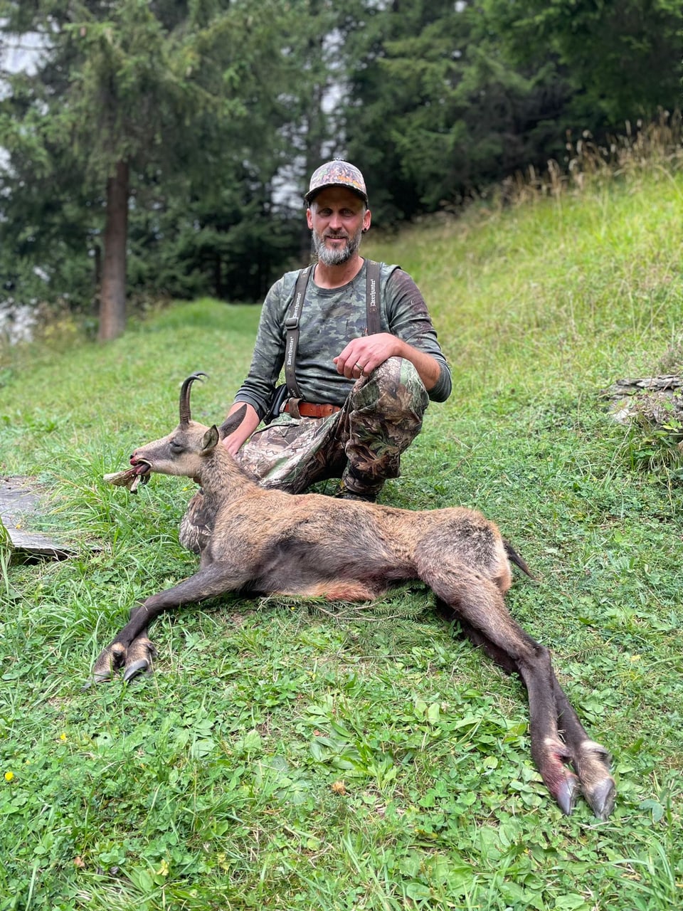 Jäger posiert mit erlegtem Hirsch in waldiger Umgebung.