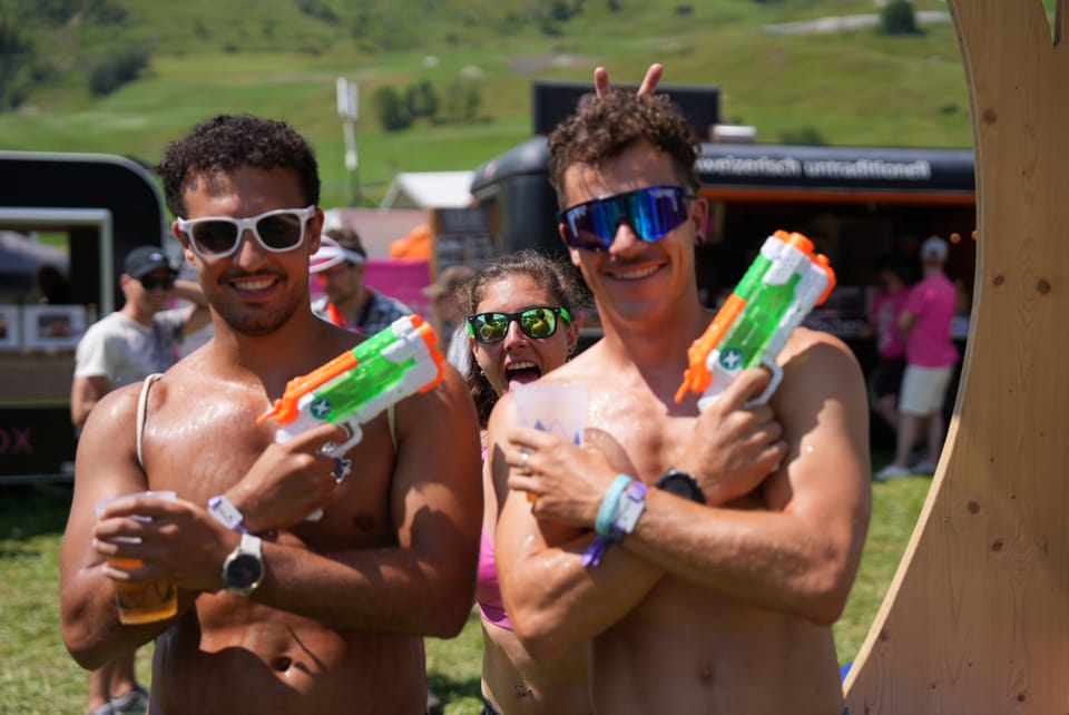 Drei lachende Erwachsene mit Wasserpistolen auf einem Outdoor-Festival.
