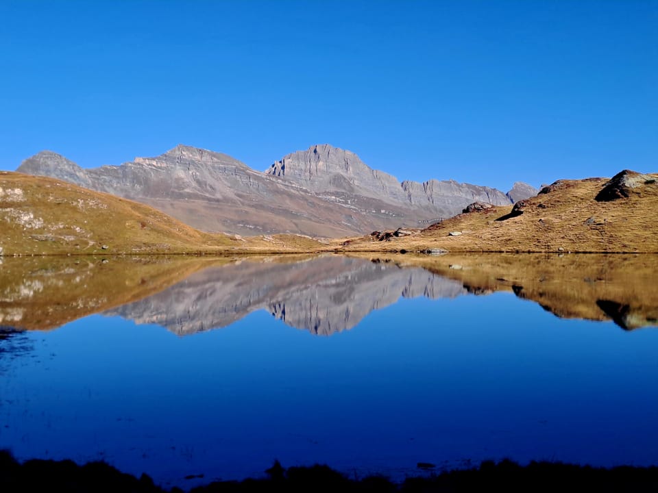 Spiegelung von Bergen in einem klaren See unter blauem Himmel.