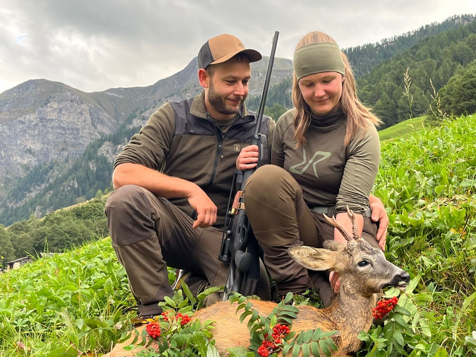 Zwei Jäger posieren mit einem erlegten Reh in einer Berglandschaft.