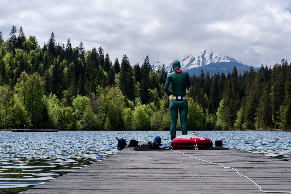 Person in Taucheranzug auf Steg mit Bergkulisse